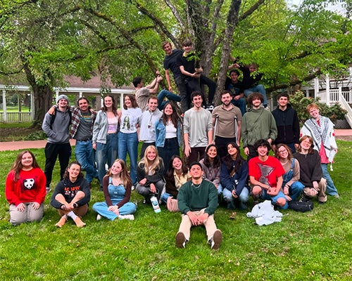 Students sitting and standing in front of a tree with several of them climbing it